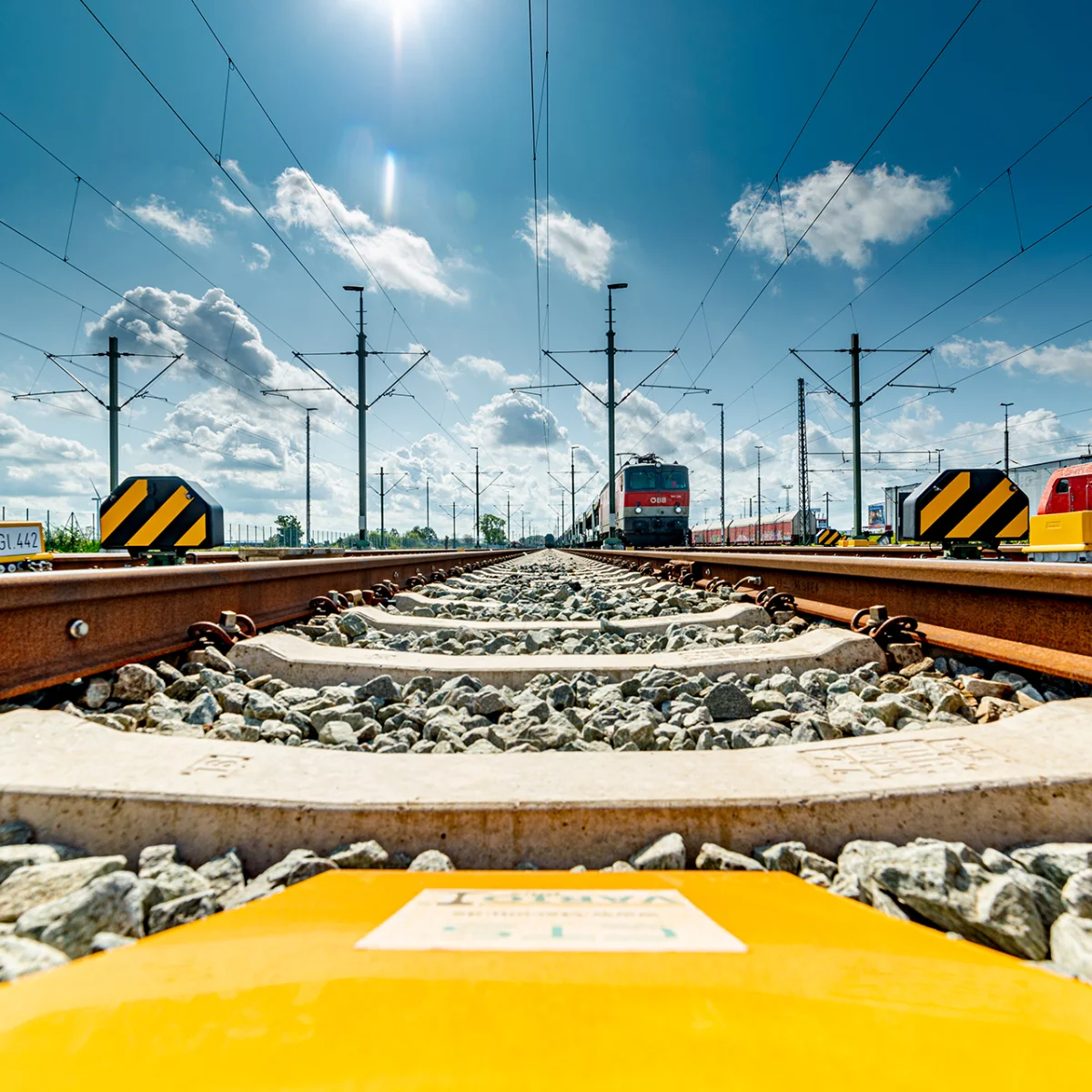 Nahaufnahme von Bahngleisen mit Oberleitungen und Zügen der Deutschen Bahn bei Sonnenschein – steht für Technik, Präzision und Zukunftsperspektiven bei ai Consult GmbH.